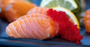 Close-up of fresh salmon sashimi topped with bright red caviar and garnished with lemon slices.