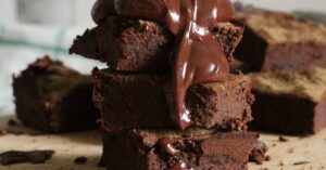 Delicious stack of chocolate brownies drizzled with gooey syrup on a wooden board.