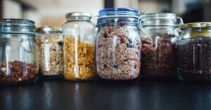 Close-up of various cereals in glass jars on a kitchen counter, showcasing diverse breakfast options.