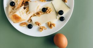 A stylish breakfast plate featuring cheese, walnuts, olives, and bread on a green background.